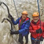 1. Two elderly men ice climbing on a frozen waterfall, wearing helmets and jackets.