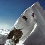 Climber ascending a snow-covered mountain peak in extreme outdoor adventure, high-altitude mountaineering.