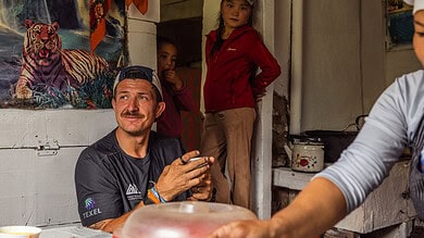 Children observing man inside a rustic wooden home in a rural setting.