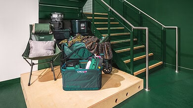 Aluminium green staircase with outdoor gear and camping equipment on wooden platform.