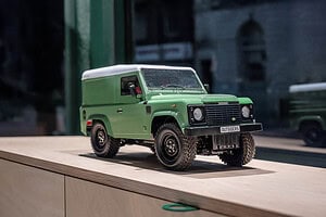 Green Land Rover Defender toy model on a wooden surface outdoors Campervan replica for outdoor adventure and camping enthusiasts.