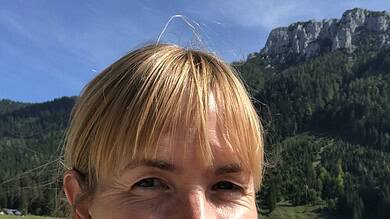 Bright woman hiking outdoors with green mountains and blue sky in the background, enjoying nature.