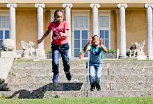 Children jumping down stone steps in front of a historic building with classical columns, outdoor activity, family fun, outdoor exploration, outdoor adventure.