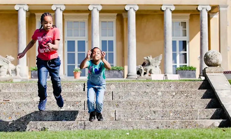 Children jumping down stone steps in front of a historic building with classical columns, outdoor activity, family fun, outdoor exploration, outdoor adventure.