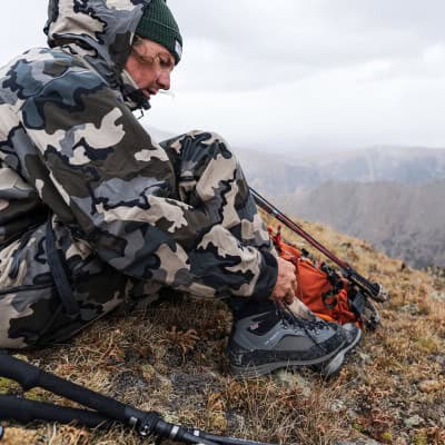 Camo outdoor hiking jacket and gear on mountain trail in wilderness.