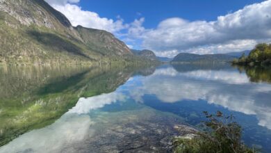 Serene mountain lake landscape with clear water, lush green hills, and blue sky, perfect for outdoor adventure and nature exploration.