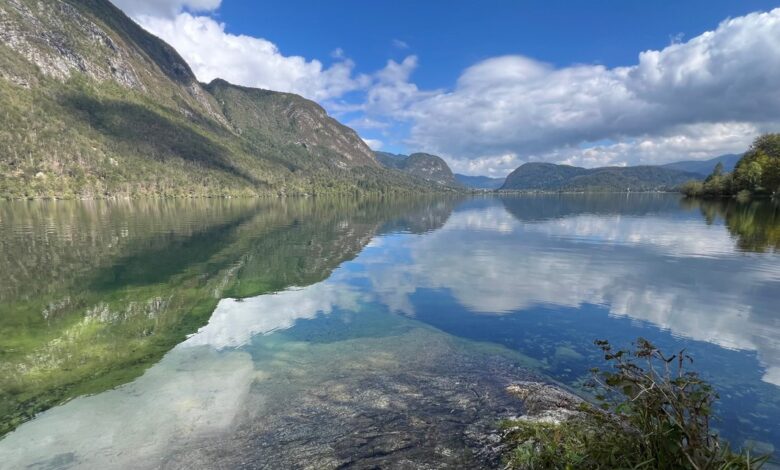Serene mountain lake landscape with clear water, lush green hills, and blue sky, perfect for outdoor adventure and nature exploration.