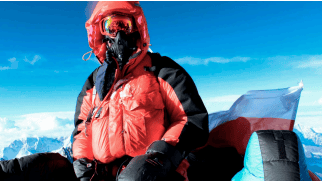 High-altitude mountaineer in red gear on snowy mountain peak with clear blue sky.