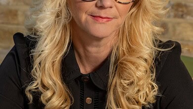 Elegant woman wearing fashionable eyeglasses, natural light, brick wall background, representing outdoor lifestyle.