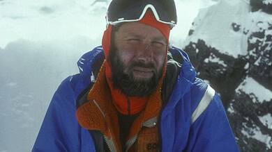 High-altitude mountaineer in cold weather gear on snow-capped mountain peak.