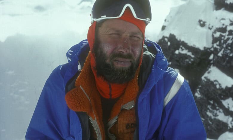 High-altitude mountaineer in cold weather gear on snow-capped mountain peak.