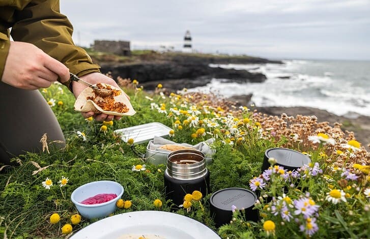 Fresh outdoor picnic setup with sandwiches, flowers, and seaside view at Lighthouse Cove.
