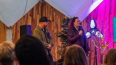 People speaking at an outdoor event or seminar in a wooden venue with colourful lighting.