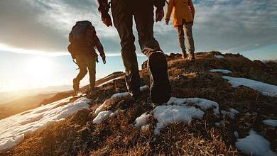 Adventurous hikers trekking on rugged mountain trail in snow and daylight.