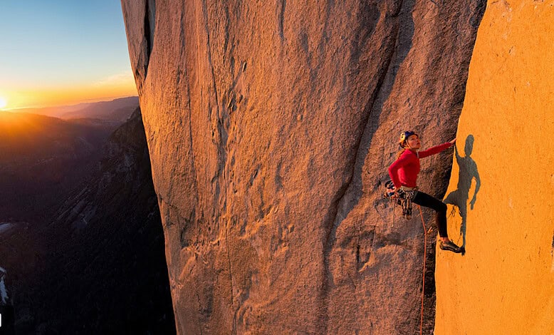 Stunning female rock climber at sunset on a mountainside in outdoor adventure setting.