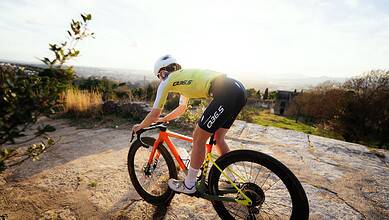 Cyclist riding a mountain bike on rocky terrain with scenic views in the background.
