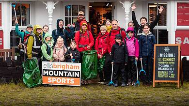 Group of hikers with backpacks outside a shop, smiling and waving.