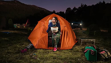 Woman sitting outside an orange tent during night camping.