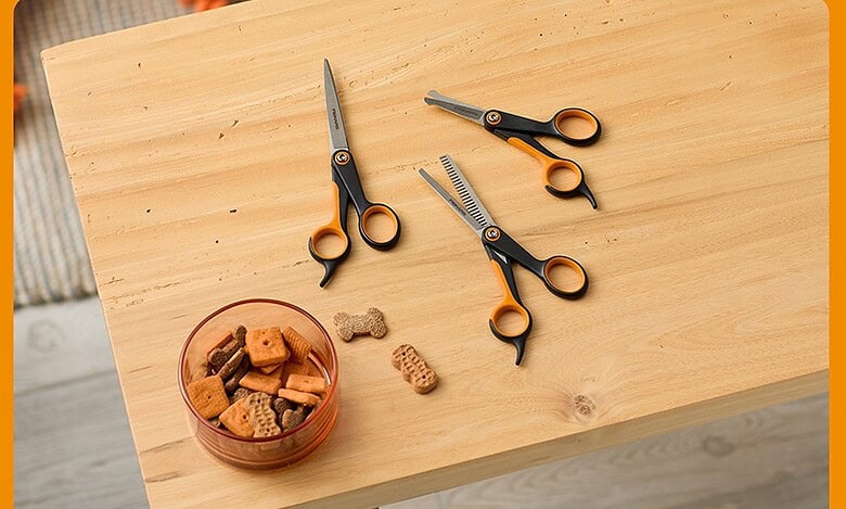 Grooming scissors and pet care tools for dogs on a wooden table with treats.