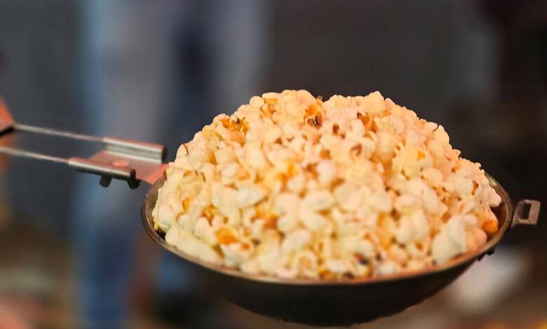 Popcorn served in a black bowl at an outdoor event, with people and warm lighting in the background.