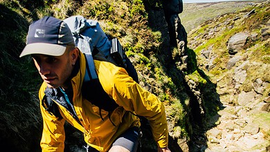 Man hiking on rocky trail with backpack in outdoor landscape.