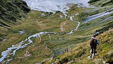 Hiker exploring a lush green mountain trail with streams and scenic views.