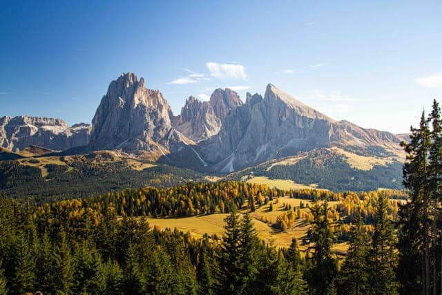 A landscape view of rugged mountain peaks with lush green forests and rolling hills under a clear bl.