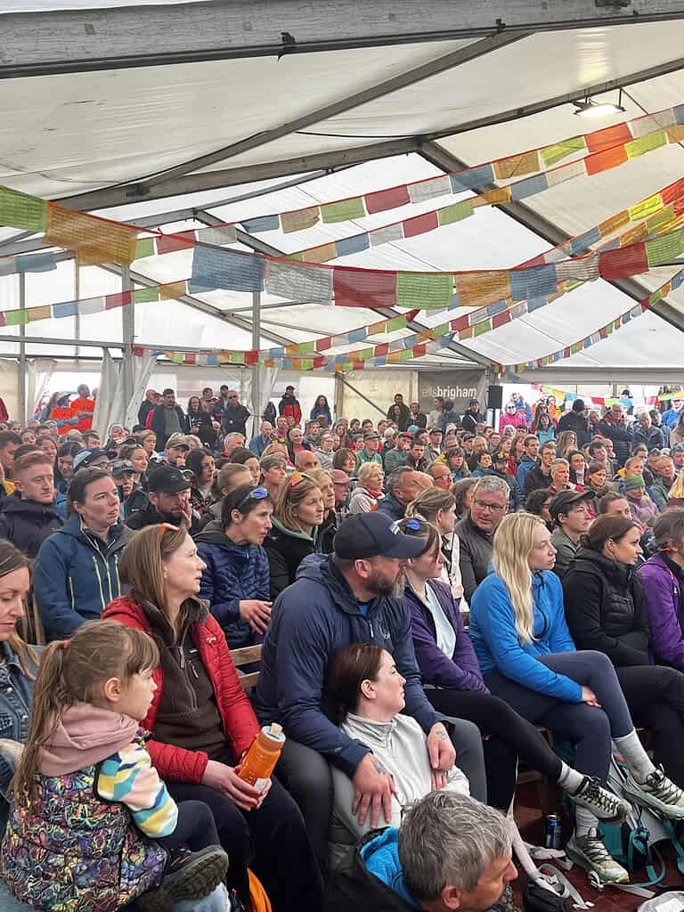 Large crowd gathered under a decorated outdoor event tent in the UK.