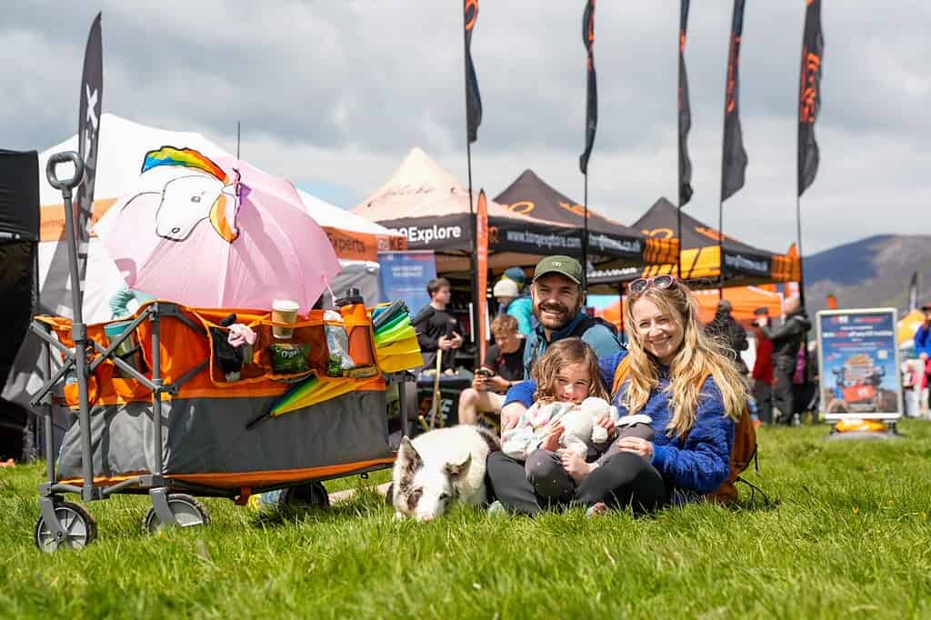 Family enjoying outdoor camping at a festival with tents and flags in the background.