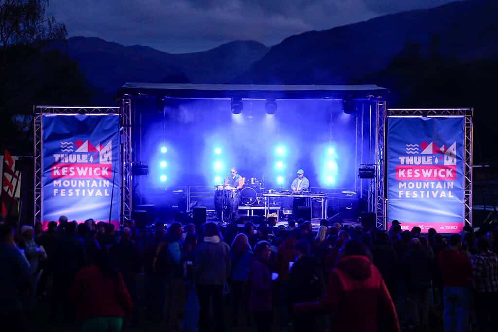 Outdoor concert at KESWICK Mountain Festival with stage lighting and audience in scenic mountain set.