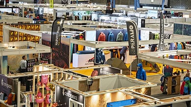 Indoor outdoor gear trade show with various booths and visitors.