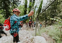 Climber securing safety rope in forest during outdoor adventure activity.