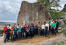 Group of hikers and outdoor enthusiasts in front of a large rock formation.