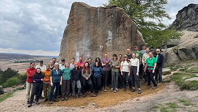 Group of hikers and outdoor enthusiasts in front of a large rock formation.
