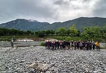 Outdoor group hike by river in scenic mountain landscape.