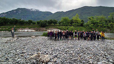 Outdoor group hike by river in scenic mountain landscape.