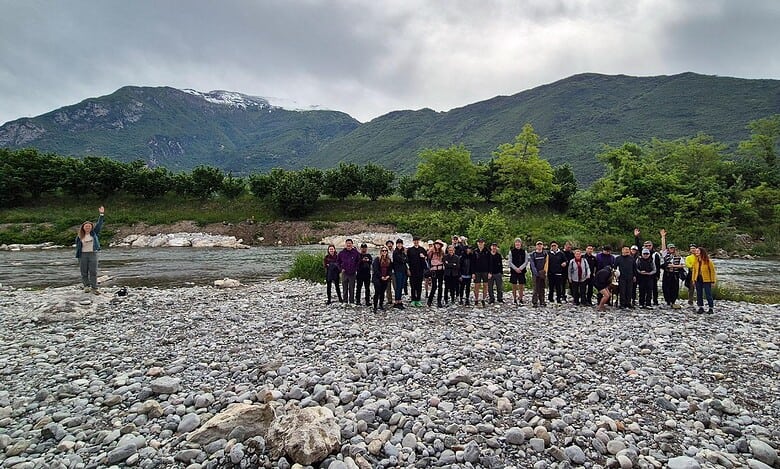 Outdoor group hike by river in scenic mountain landscape.
