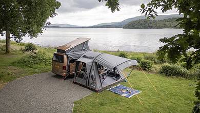 Family camping setup with tent and car near a lake in a scenic outdoor location.