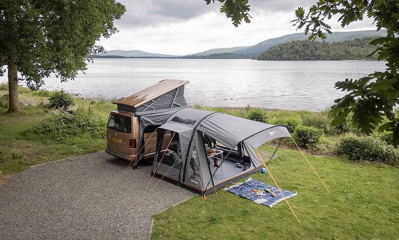 Family camping setup with tent and car near a lake in a scenic outdoor location.