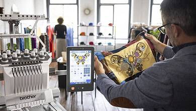Man using embroidery machine with tablet in a craft shop.
