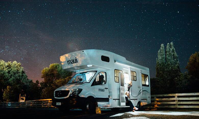 Motorhome parked under a starry night sky with trees and a wooden fence nearby.