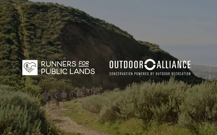 Hikers walking along a trail near a green hillside with logos for Runners for Public Lands and OutdO.
