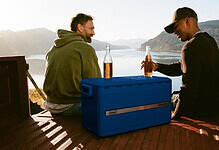 Two men enjoying a picnic by a lake with scenic mountain views.