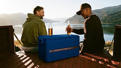 Two men enjoying a picnic by a lake with scenic mountain views.