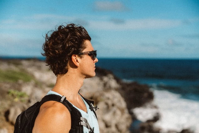 Young man with backpack enjoying coastal hike on a sunny day.