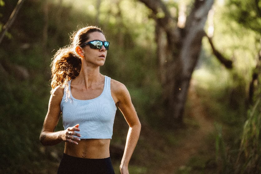 Woman running outdoors in sportswear with sunglasses in nature.