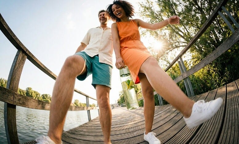 Happy young couple enjoying outdoor walk on a wooden bridge by a lake.