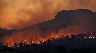 Wildfire burning on mountain with smoke and flames in the evening.
