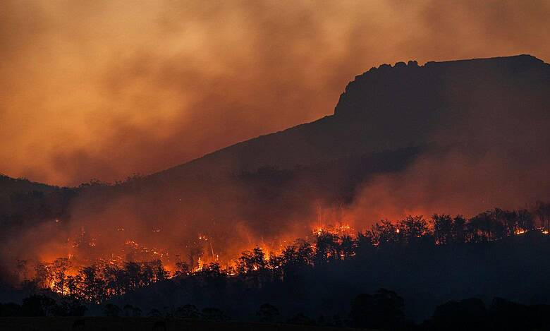 Wildfire burning on mountain with smoke and flames in the evening.