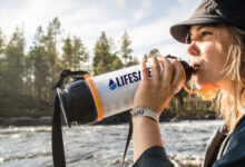 Person drinking from a LifeSaver bottle beside a river